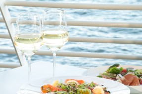 Photo: Two wine glasses with drinks and a plate of food on a balcony table