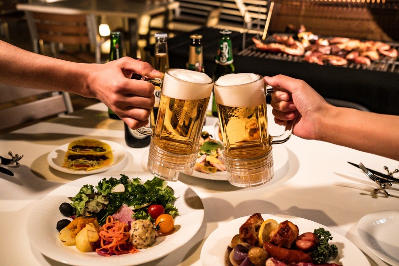 写真：ビーフロティやタコスなどのお料理の上でビールジョッキで乾杯する様子