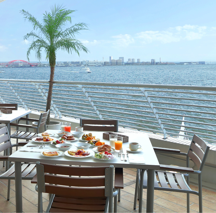 写真：昼の港の景色を背景にテラス席には朝食が並んでいる