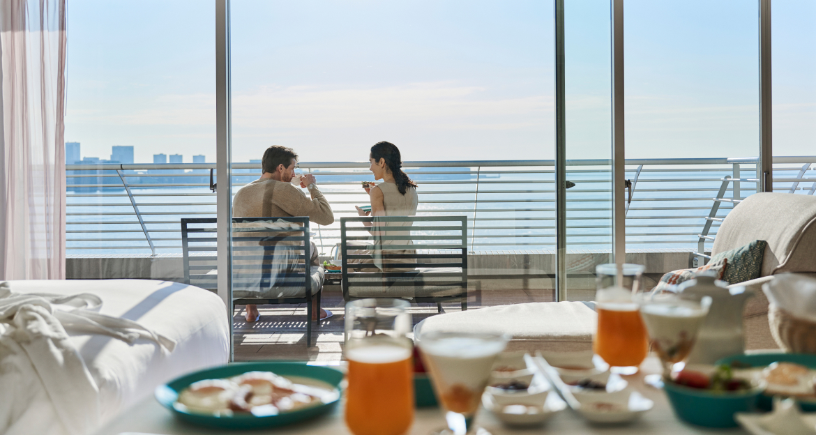 写真：客室のテーブルの上には朝食が並び、バルコニー席で朝食を楽しむカップル