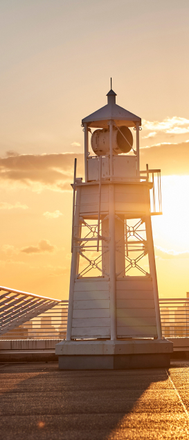 写真：夕日を背景にして立つ白い灯台