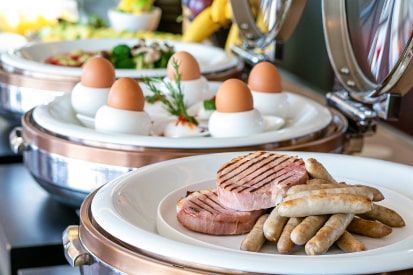 写真：ビュッフェスタイルの朝食で、ソーセージとハム、茹で卵が並んでいる